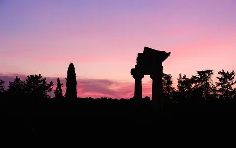 Silhouette eines antiken Tempels vor einem violett-rosa Abendhimmel