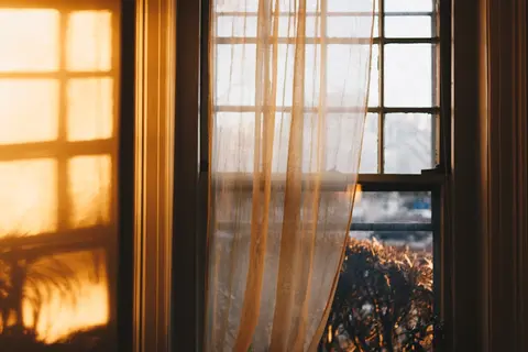 Warmes goldenes Licht faellt durch einen halbtransparenten Vorhang