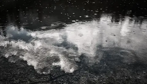 Raindrops falling on a water surface reflecting the sky.
