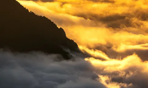 Mountain peak emerging from golden clouds at sunrise.