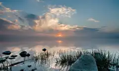 Sunrise over a calm misty lake with rocks.