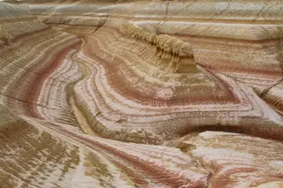 Geschichtete Gesteinsformationen mit farbigen geschwungenen Sedimentschichten in warmen Erdtönen