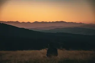 Silhouette einer einzelnen Gestalt vor einem Sonnenuntergang ueber Bergen