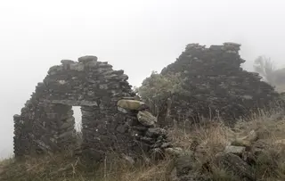 Verfallene Steinstrukturen auf einem nebligen Huegel mit trockenem Gras das durch die Ueberreste waechst