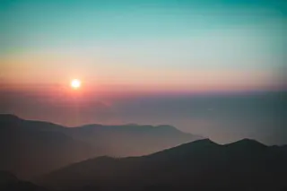 Einzelner Baum auf einem Huegel bei Sonnenaufgang mit weitem Blick ueber nebelbedeckte Taeler